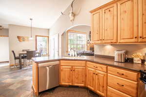 Kitchen with stainless steel appliances, light brown cabinets, a peninsula, decorative light fixtures, and vaulted ceiling