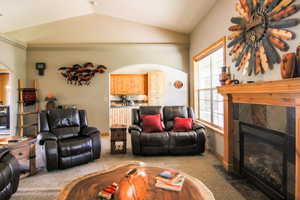 Living room with arched walkways, vaulted ceiling, carpet floors, and a fireplace