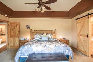 Bedroom with a barn door, connected bathroom, carpet, and a ceiling fan