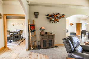Living area featuring arched walkways, a chandelier, crown molding, and light wood-style floors