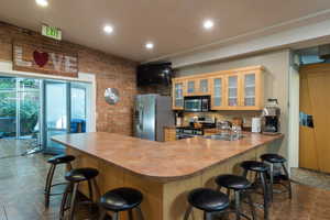 Kitchen with glass insert cabinets, brick wall, a kitchen breakfast bar, dark tile patterned floors, and appliances with stainless steel finishes