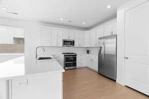 Kitchen with appliances with stainless steel finishes, white cabinetry, a peninsula, light wood-type flooring, and recessed lighting