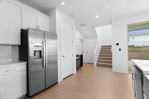 Kitchen with stainless steel refrigerator with ice dispenser, light wood-style floors, recessed lighting, and white cabinets