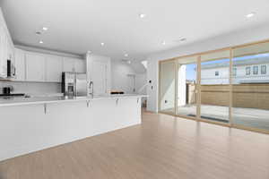 Kitchen featuring a kitchen bar, white cabinetry, stainless steel fridge, light wood-style flooring, and recessed lighting