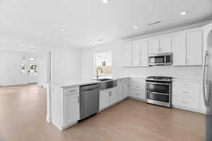 Kitchen featuring appliances with stainless steel finishes, white cabinetry, a peninsula, recessed lighting, and light wood-style floors