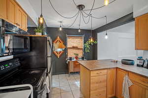 Kitchen with black appliances, hanging light fixtures, a peninsula, light tile patterned flooring, and light brown cabinetry