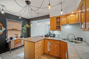 Kitchen featuring hanging light fixtures, glass insert cabinets, a peninsula, light tile patterned flooring, and tasteful backsplash