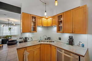 Kitchen featuring pendant lighting, stainless steel dishwasher, decorative backsplash, and tile countertops