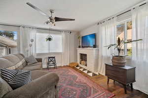 Living room featuring wood finished floors, a fireplace, and ceiling fan