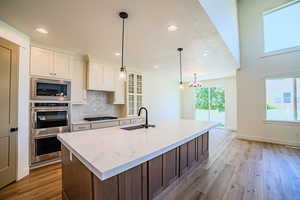 Kitchen with recessed lighting, tasteful backsplash, light wood-style flooring, glass insert cabinets, and hanging light fixtures