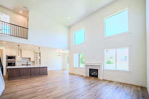 Unfurnished living room with light wood finished floors, a towering ceiling, recessed lighting, a fireplace, and a chandelier