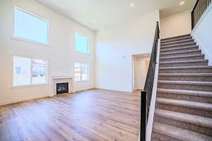 Unfurnished living room featuring stairs, recessed lighting, a high ceiling, light wood-type flooring, and a fireplace