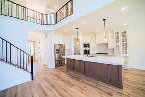 Kitchen with recessed lighting, a towering ceiling, an island with sink, stainless steel appliances, and dark brown cabinets