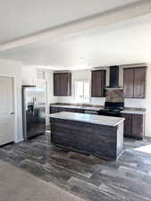Kitchen featuring dark brown cabinetry, stainless steel appliances, a kitchen island, wall chimney exhaust hood