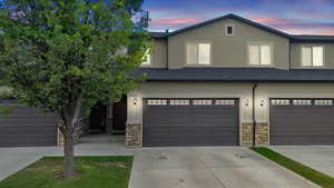 View of front of home featuring stone siding, driveway, stucco siding, roof with shingles, and a garage