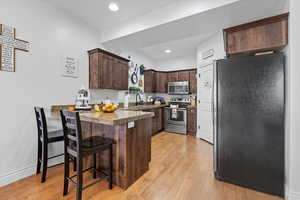 Kitchen featuring dark brown cabinets, stainless steel appliances, a peninsula, light wood-style floors, and a breakfast bar area