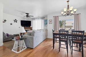 Dining area featuring light wood-type flooring, a ceiling fan, a tile fireplace, and a chandelier