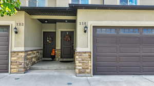 Entrance to property with stone siding, stucco siding, a garage, and covered porch