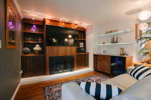 Living area with crown molding, wine cooler, light wood-type flooring, and a large fireplace