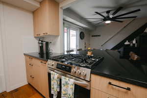 Kitchen featuring light brown cabinets, gas stove, a ceiling fan, dark wood-style floors, and dark stone counters
