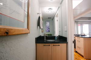 Bar area featuring range with gas stovetop, a textured wall, light wood finished floors, light brown cabinets, and dark stone countertops