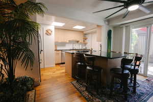 Kitchen featuring dark countertops, light wood-type flooring, a ceiling fan, a breakfast bar, and open shelves