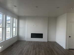 Unfurnished living room with dark wood-style flooring, a glass covered fireplace, and a textured ceiling