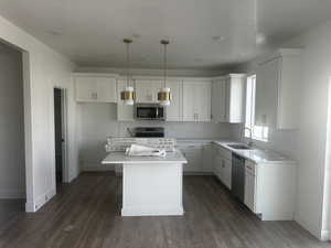 Kitchen with white cabinets, decorative backsplash, a center island, hanging light fixtures, and dark wood-type flooring