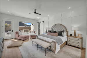 Bedroom featuring a barn door, recessed lighting, light wood-style floors, ceiling fan, and a decorative wall