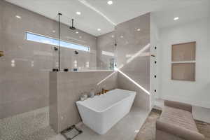 Bathroom featuring a freestanding bath, walk in shower, recessed lighting, and tile walls