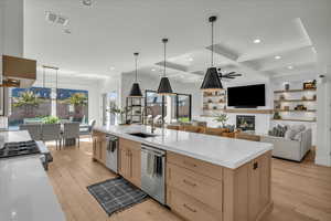 Kitchen with light brown cabinets, pendant lighting, light stone countertops, beam ceiling, and light wood-style floors