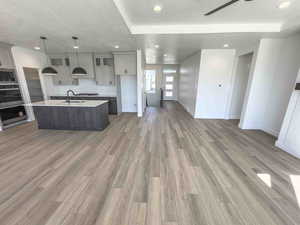 Kitchen featuring open floor plan, a textured ceiling, an island with sink, pendant lighting, and dark wood-style floors