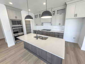 Kitchen featuring tasteful backsplash, light stone countertops, a center island with sink, pendant lighting, and recessed lighting