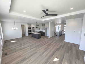 Kitchen with open floor plan, a tray ceiling, an island with sink, a chandelier, and pendant lighting