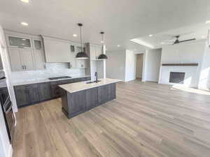 Kitchen with tasteful backsplash, a center island with sink, hanging light fixtures, a textured ceiling, and light wood-style flooring