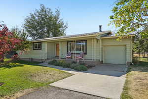 Ranch-style home featuring concrete driveway, a front yard, an attached garage, a metal roof, and a porch
