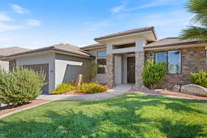 Rambler-style house featuring stucco siding, a front lawn, stone siding, and 3-car garage
