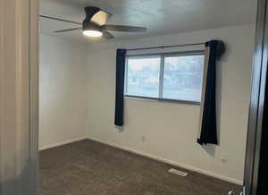 Unfurnished room featuring dark carpet, a textured ceiling, and a ceiling fan