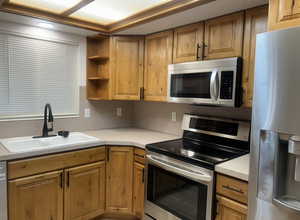 Kitchen with appliances with stainless steel finishes, open shelves, brown cabinetry, and light countertops