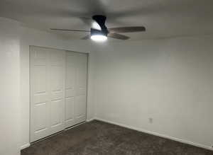 Unfurnished bedroom featuring a closet, dark carpet, and a ceiling fan