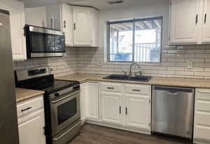 Kitchen featuring stainless steel appliances, white cabinets, backsplash, dark wood finished floors, and light stone counters
