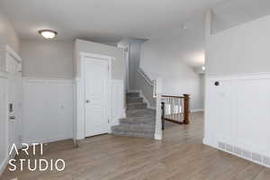 Foyer with stairs, a decorative wall, light wood-style flooring, and wainscoting