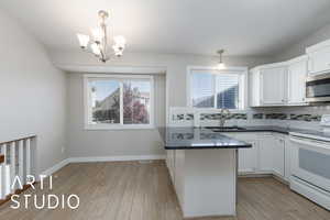 Kitchen featuring tasteful backsplash, electric stove, decorative light fixtures, a peninsula, and white cabinets