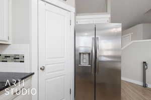 Kitchen featuring stainless steel fridge, white cabinets, tasteful backsplash, light wood-type flooring, and dark stone counters