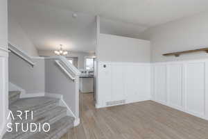 Foyer entrance featuring stairs, a chandelier, light wood-style floors, a decorative wall, and wainscoting