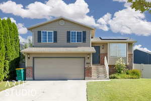 View of front of house featuring brick siding, an attached garage, driveway, solar panels, and roof with shingles