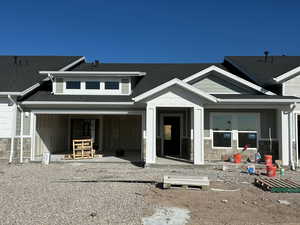 View of front facade with stone siding, a patio area, and a shingled roof