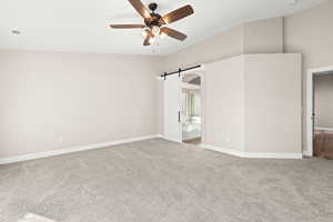 Empty room with a barn door, light carpet, and ceiling fan