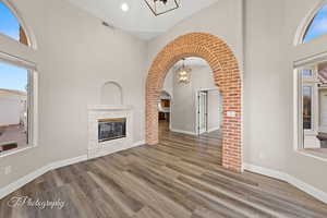 Unfurnished living room featuring a high ceiling, arched walkways, a fireplace, a chandelier, and wood finished floors