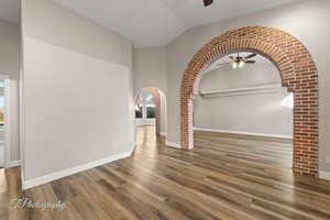 Empty room with arched walkways, ceiling fan, wood finished floors, and high vaulted ceiling